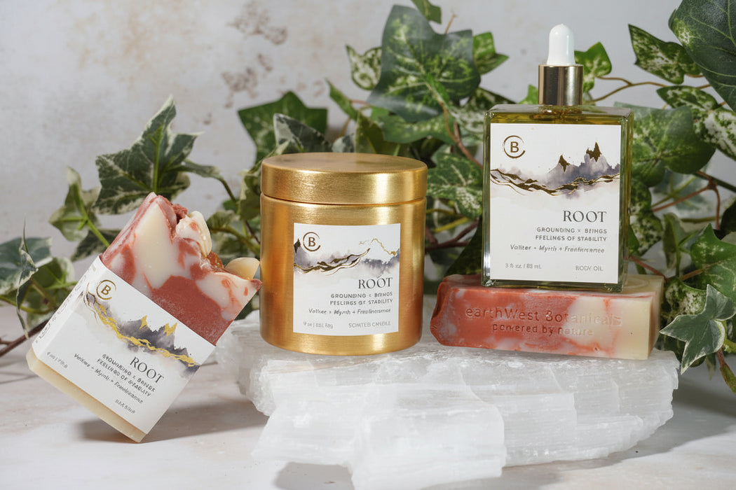 ROOT Centers Collection including a candle, soap, and body oil with a label on a stone surface with greenery in the background.