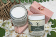 Jar of body butter with a pink soap bar on a textured surface.