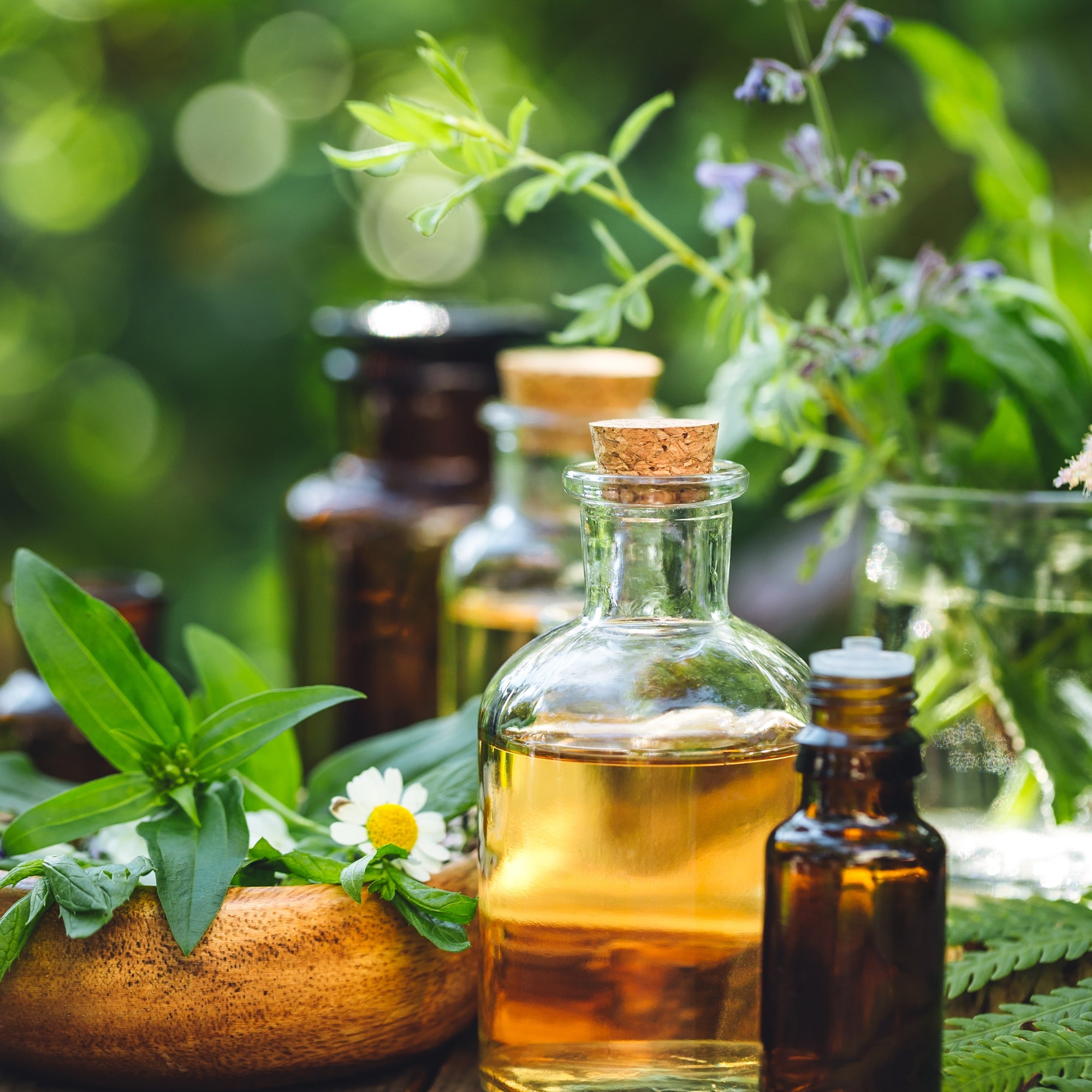 Glass bottle of oil with cork lid on a wooden surface surrounded by herbs and plants.