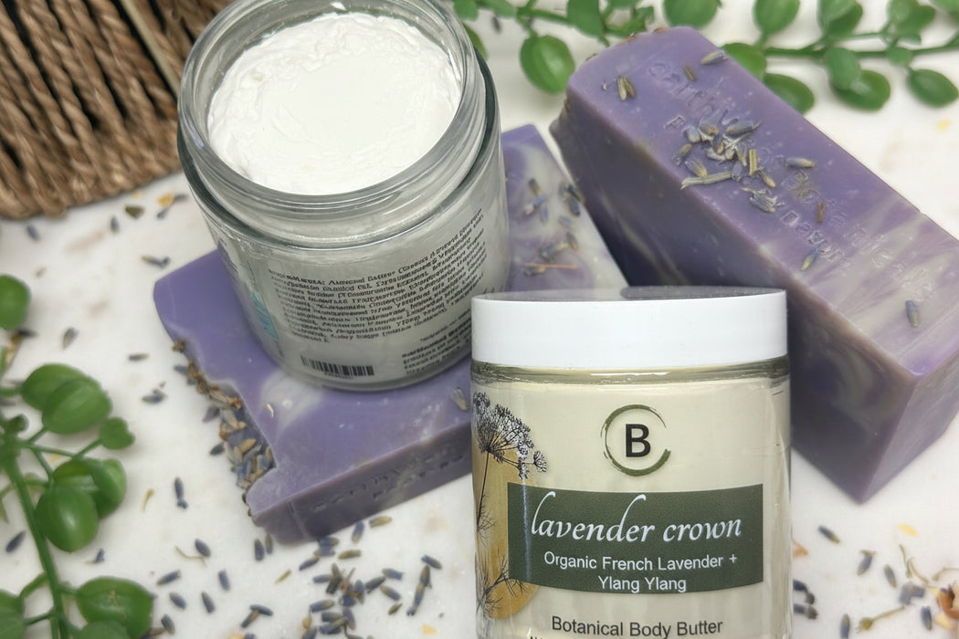 Lavender-themed skincare products including a jar of body butter, a jar of powder, and a bar of soap on a white surface with lavender leaves.