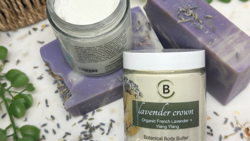 Lavender-themed skincare products including a jar of body butter, a jar of powder, and a bar of soap on a white surface with lavender leaves.