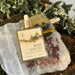 Two bottles of 'Root' body oil on a textured stone surface with plants in the background