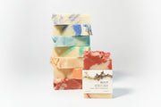 Stack of colorful soap bars with a single labeled Root bar soap a gray background