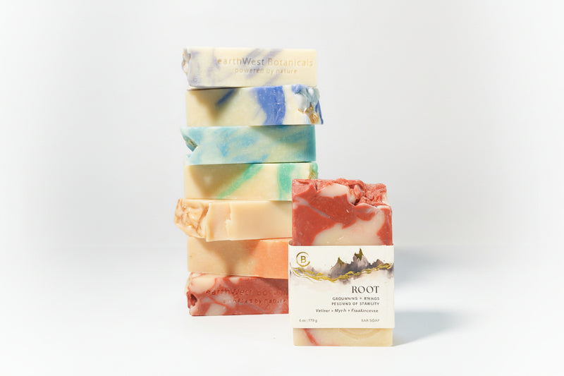 Stack of colorful soap bars with a single labeled Root bar soap a gray background