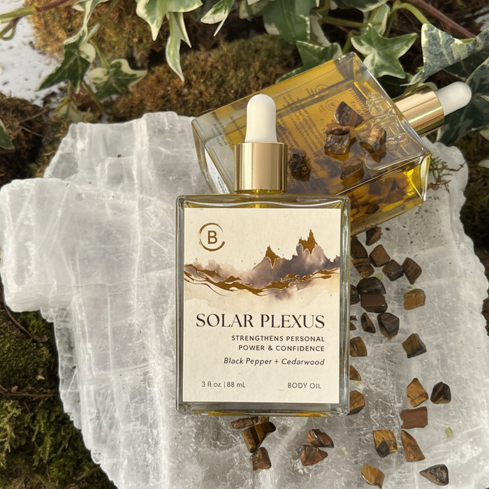 Body Oil bottle labeled 'Solar Plexus' on a crystal with plants in the background