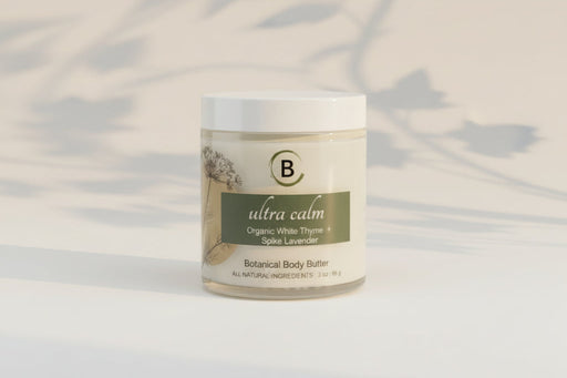 Jar of 'ultra calm' botanical body butter on a marble surface with a light gray background.