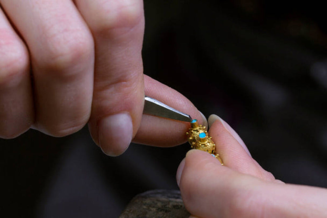 Close-up of hands working on a gold ring with a blue stone.